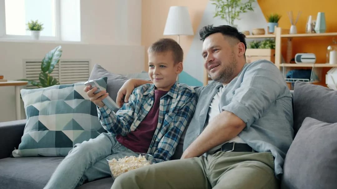 Pappa och son som tittar på TV tillsammans i soffan med popcorn